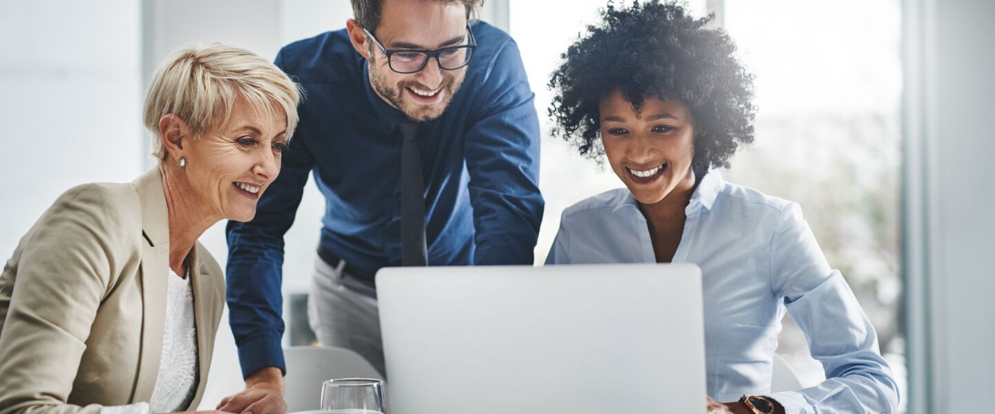 Business professionals collaborating at a desk, smiling while looking at a laptop screen, representing Voices' additional services like translation and post-production support