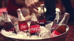 A man grabs a Coca Cola bottle from a bucket full of ice.