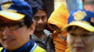 Two Rotary International workers standing in the foreground, with a father holding his child behind them.