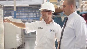 Two factory workers, one with a hard hat, studying a set of plans.