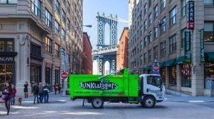 A bright green Junkluggers truck driving trough an intersection in a big city.