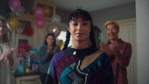 A woman standing in a room decorated for her birthday, with her friends smiling and clapping