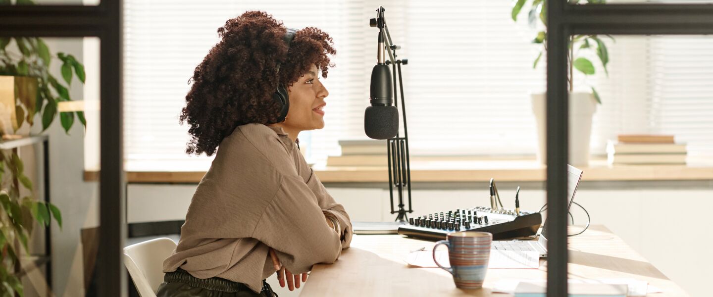 Background image of a woman wearing headphones, recording at a desk with a microphone and audio equipment, in a professional voiceover setup